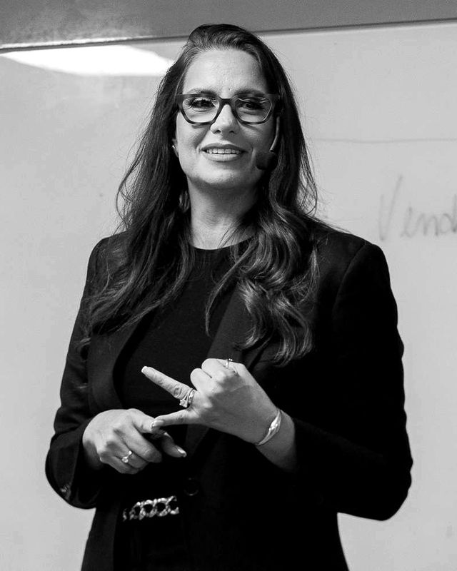 Lilian Carmo falando numa sala de treinamento, em preto e branco